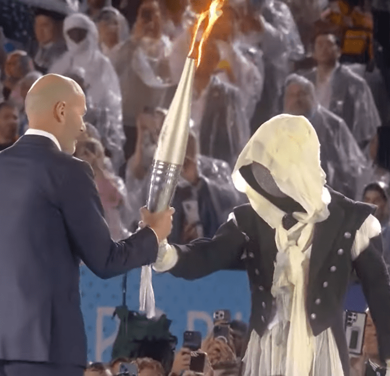 Momento na qual o misterioso mascarado passa a tocha olímpica para Zinedine Zidane na abertura da Olimpíada (Foto: Youtube/Reprodução)