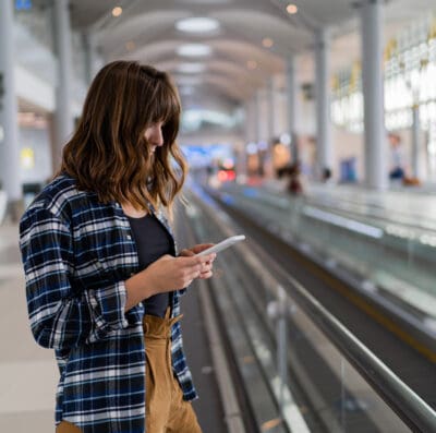 Mulher ao lado de uma esteira de aeroporto segurando seu celular.